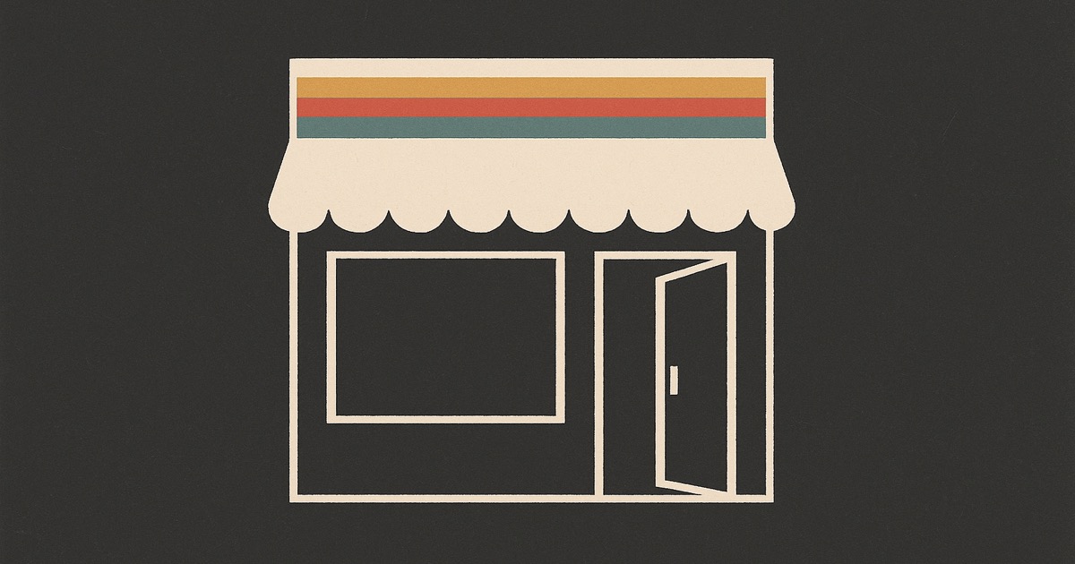 An ivory shop front with its door open and three stripes of ochre, red and teal on the awning, on charcoal